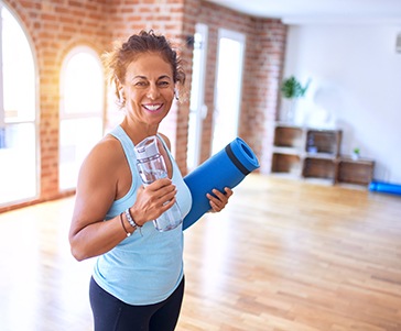 Smiling woman holding water bottle and yoga mat