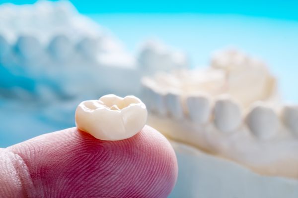 A dental crown being held on a fingertip